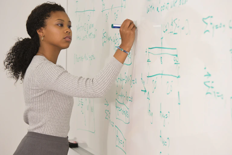 A woman does math at a whiteboard