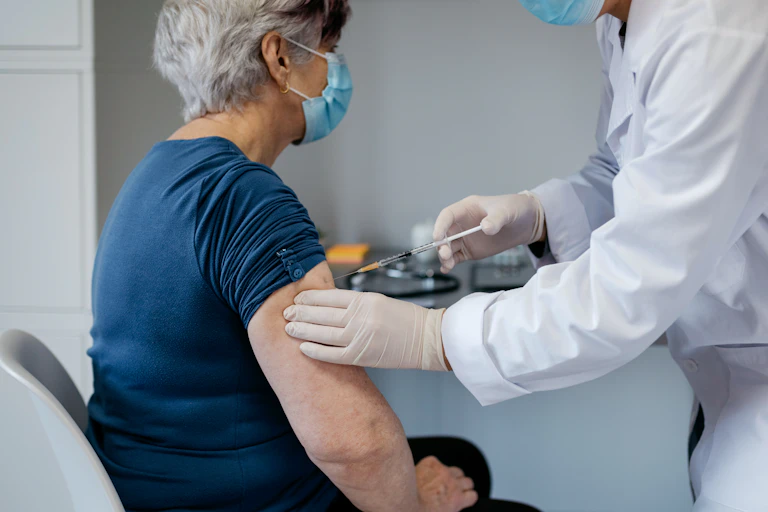 An elderly woman receives a vaccine from a doctor.