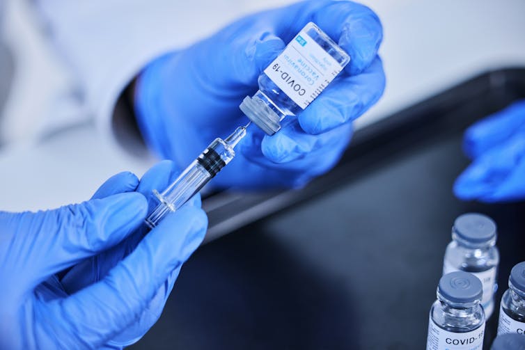 A doctor or nurse wearing blue gloves fills a syringe with COVID-19 vaccine.