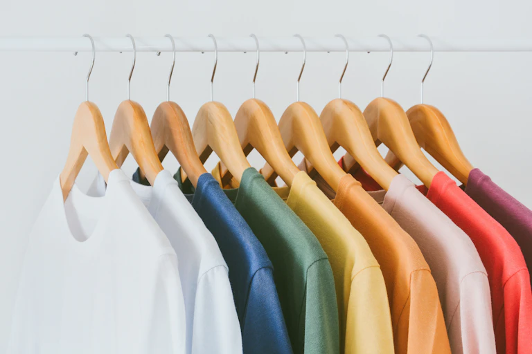 Una hilera de camisetas de colores en un perchero dispuestas en forma de arco iris.