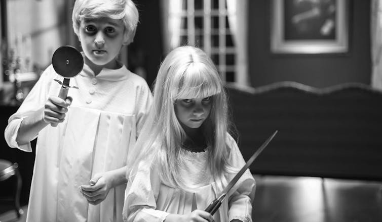 Dos niños de piel y pelos muy claros sujetan instrumentos de cocina con mirada amenazante.