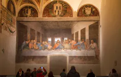 Un mural que representa a Jesucristo rodeado de los apóstoles en la última cena, pintado en una pared ante la mirada de varios visitantes.