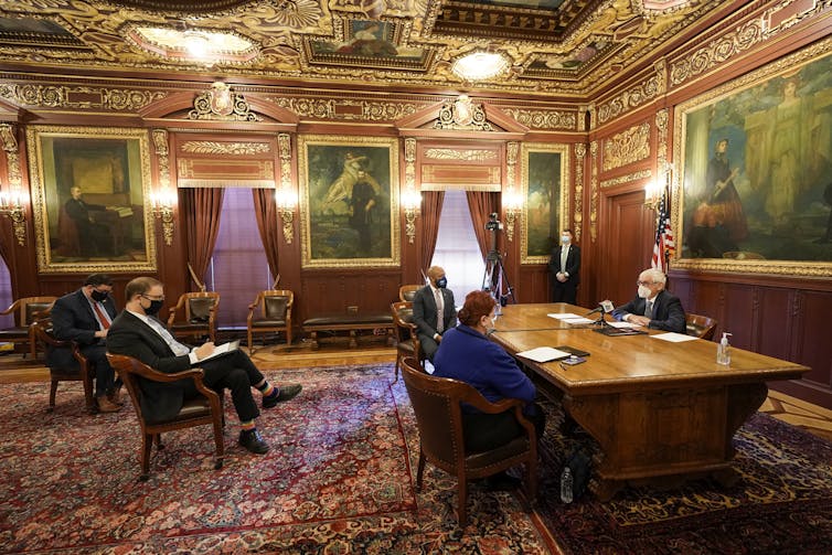 People sit in chairs in a formally decorated meeting room.