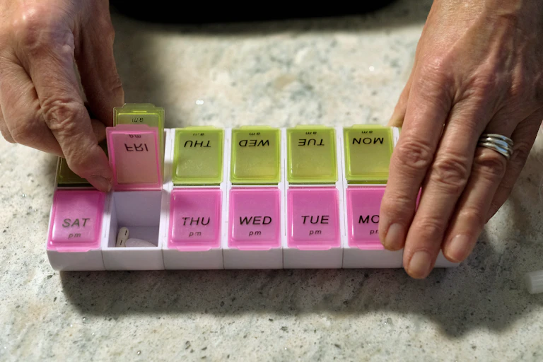 An older woman looks at a two-sided pill box for organizing daily medications.