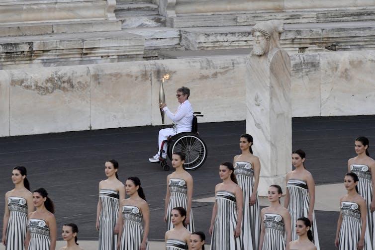 A woman in a wheelchair carries an omylpic torch as others stand nearby
