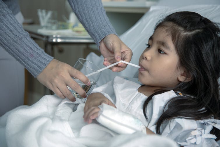 A girl in hospital drinks water through a straw.
