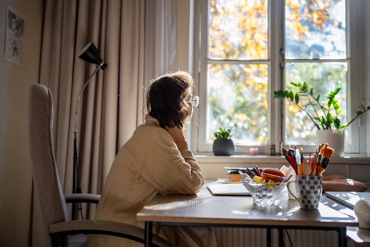 A young woman sits at a table and looks out of a window.