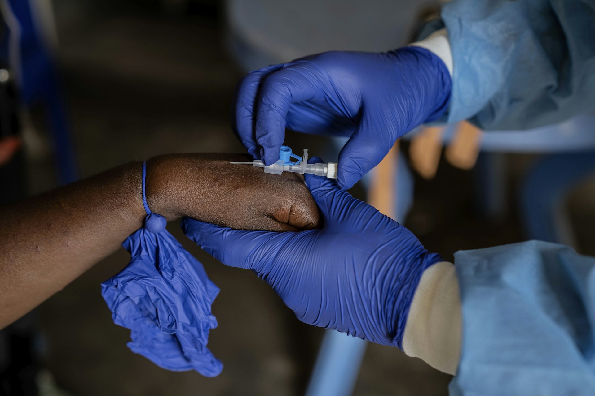 Les mains gantées d'un agent de santé insèrent une aiguille IV dans la main d'un patient