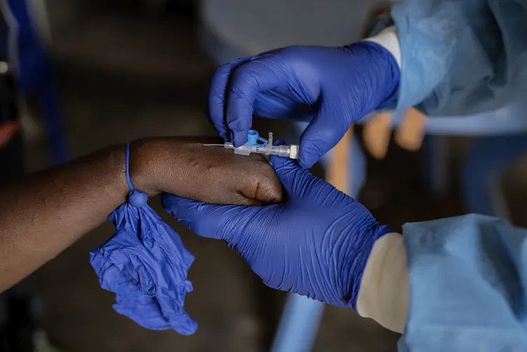Les mains gantées d'un agent de santé insèrent une aiguille IV dans la main d'un patient