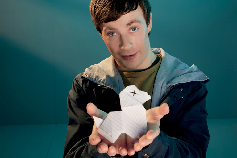 A boy wearing an anorak and holding a paper dog in outstretched hands