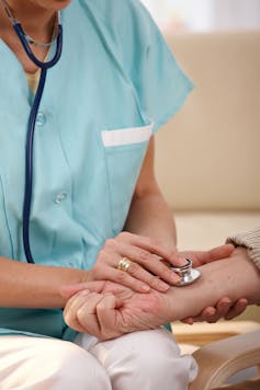 Closeup of nurse using stethoscope on wrist of senior man.