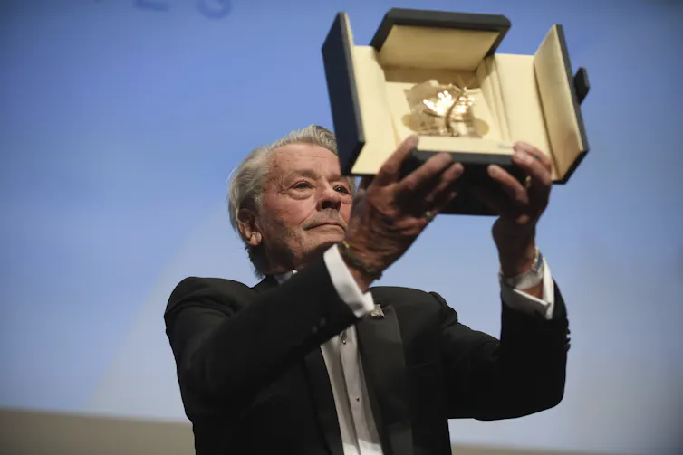 Delon sostiene su premio en alto.