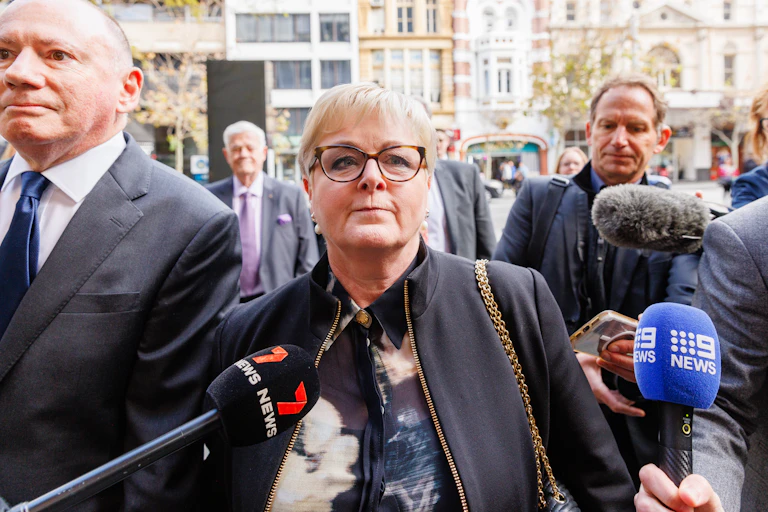 A woman walks surrounded by media and microphones