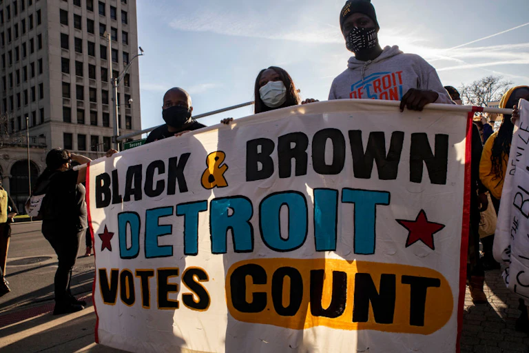 Protesters march in the streets of Detroit carrying a sign that says "Black & Brown Detroit Votes Count"