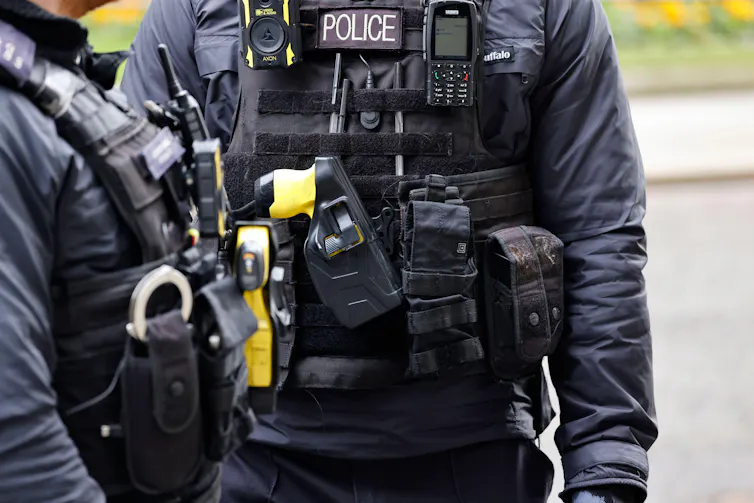 Police officers wearing body protection equipped with a radio, Taser and handcuffs.