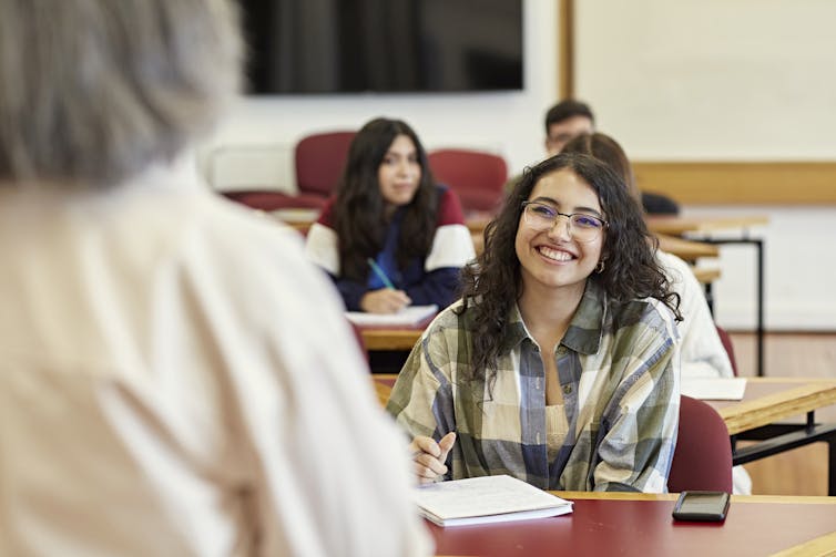 A smiling student sits at a desk looking at an instructor.