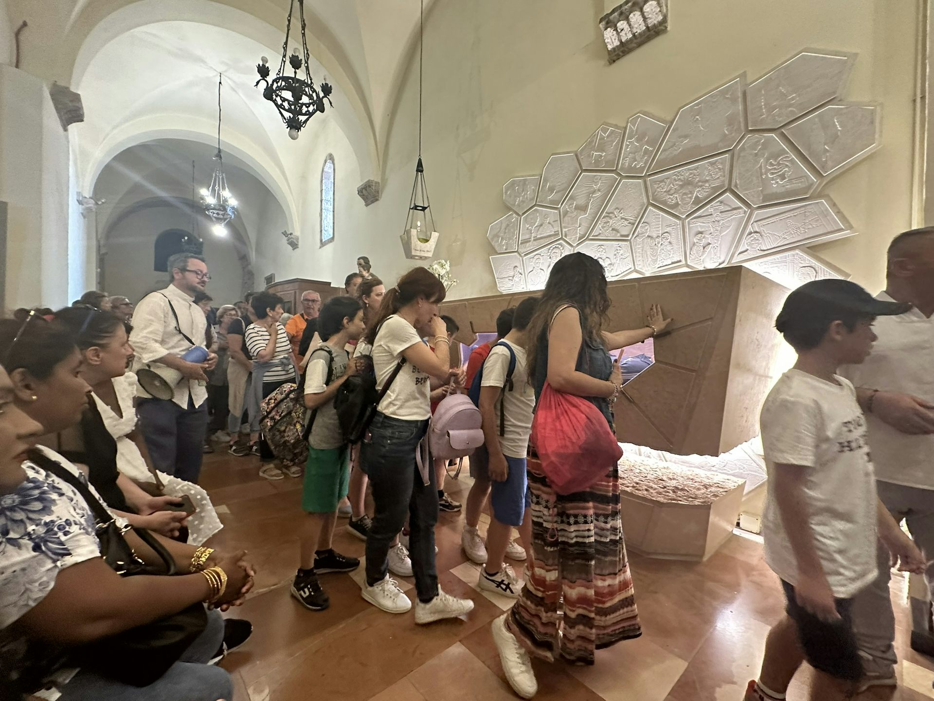 A long line of people walking past a sarcophagus, with some touching it.