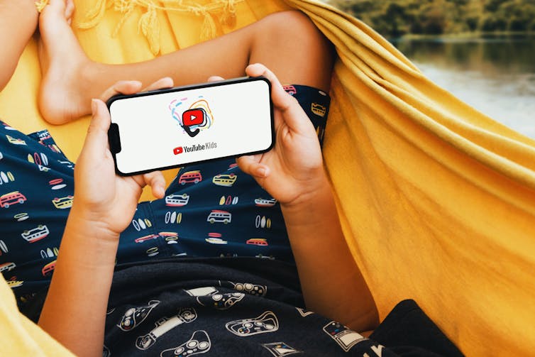 A kid has Youtube Kids open on their phone while lying in a hammock.