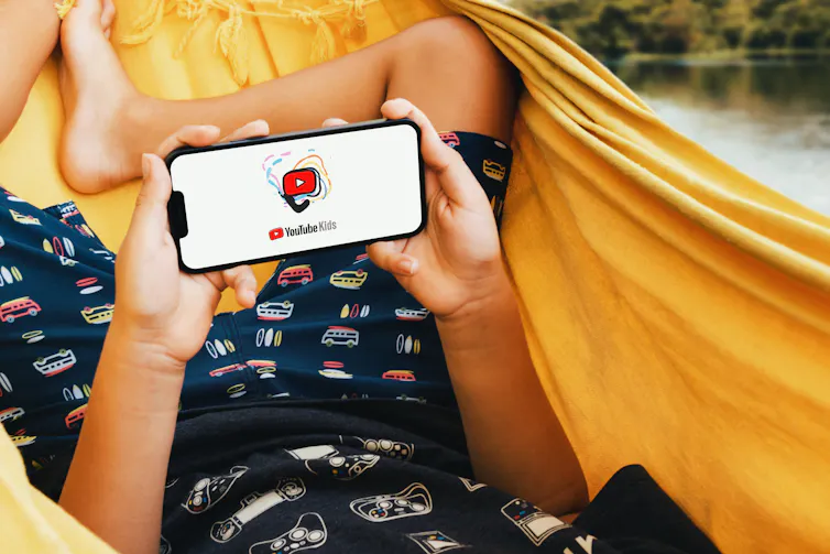 A kid has Youtube Kids open on their phone while lying in a hammock.