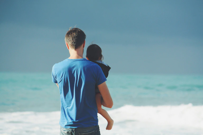 Dad holds his child, looking at the ocean