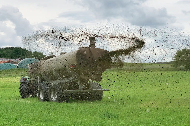 farm machine spreading dark brown animal poo into the air and across green field