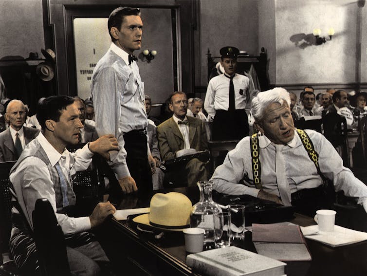A lawyer and his plaintiff sit at a table in a packed courtroom.