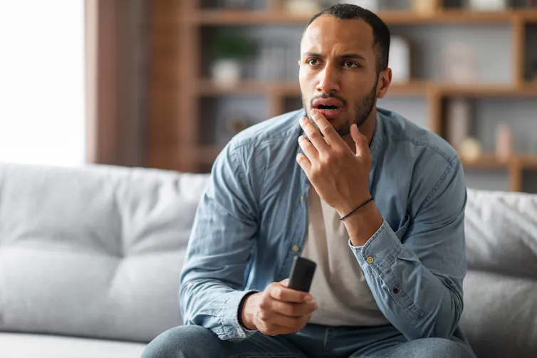 A man holds a remote control and looks confused