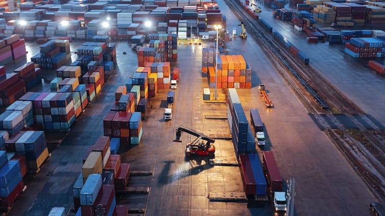 An overhead view of a fright yard, with a forklift driving between rows of large containers.
