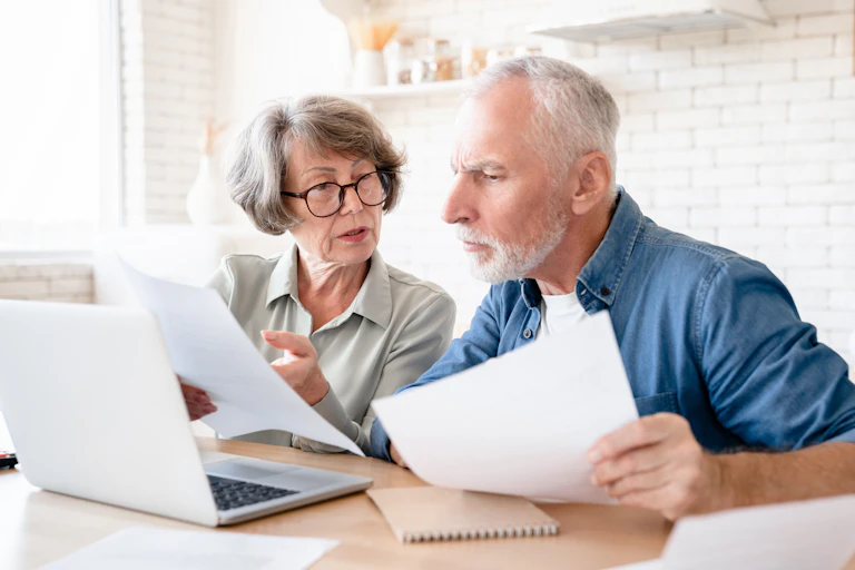 Older couple discuss their pension plans sitting at table with laptop
