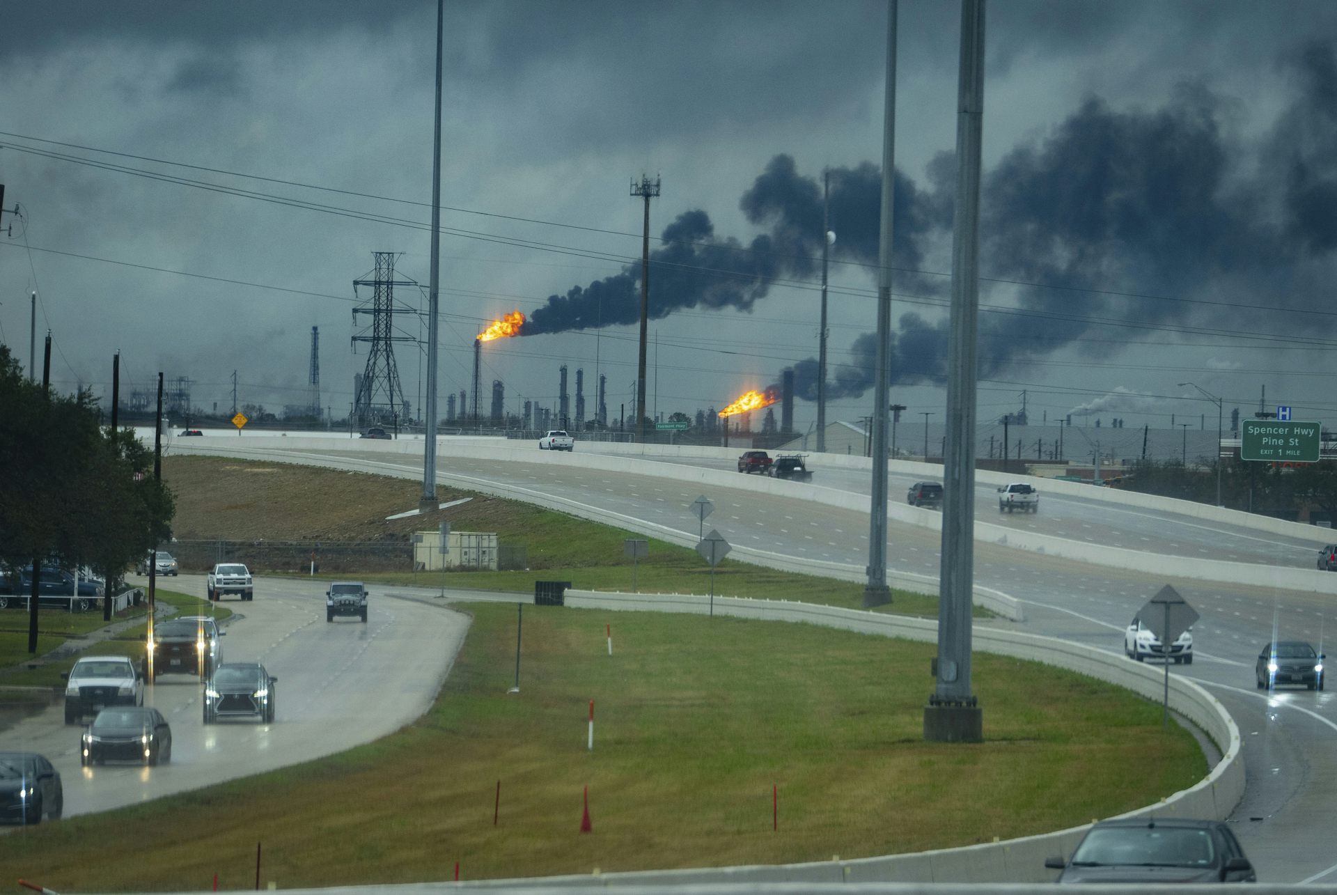 Flares burn from smokestacks near a highway.