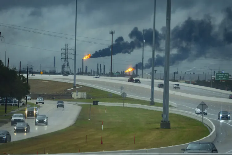 Flares burn from smokestacks near a highway.