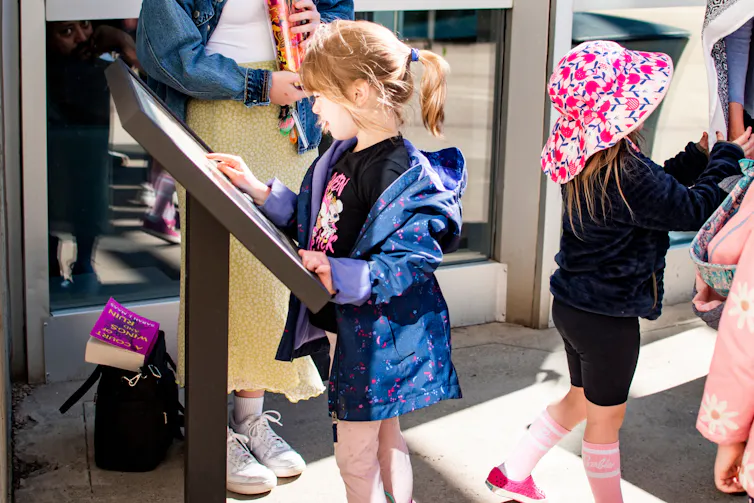 A child seen reading a plaque with adults around them.