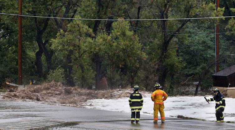 Firefighters watch a raging stream that washed out a road in Colorado.