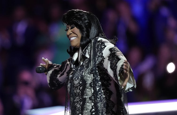 A Black woman performs in front of a large crowd.