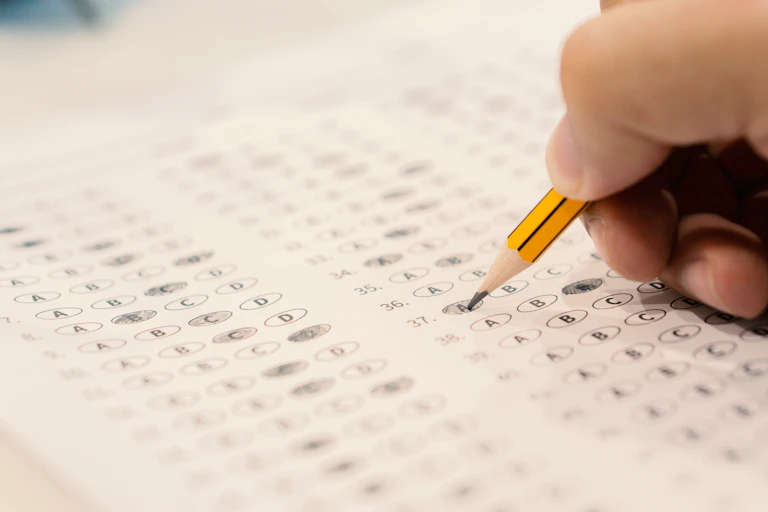 A hand holding a pencil colours in answers on a multiple choice sheet.