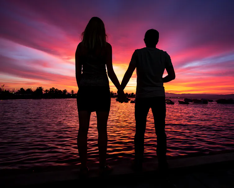 A tall woman and her partner are silhoutted against the sunset.