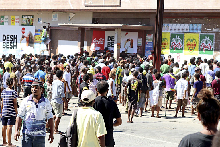 People gather a closed shopping center as a looter climbs, top left, in attempt to gain access in Port Moresby, Papua New Guinea, Wednesday, Jan. 10, 2024, after at least 15 people were reportedly killed during rioting and looting.