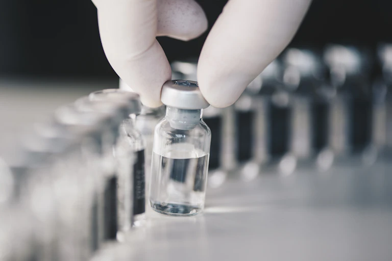 Gloved fingers holding a small bottle of clear liquid