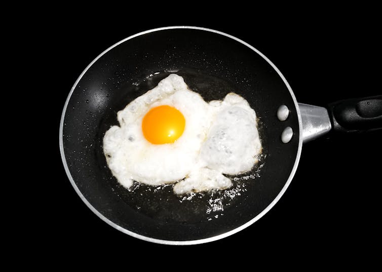 black frying pan, single friend egg, dark background.