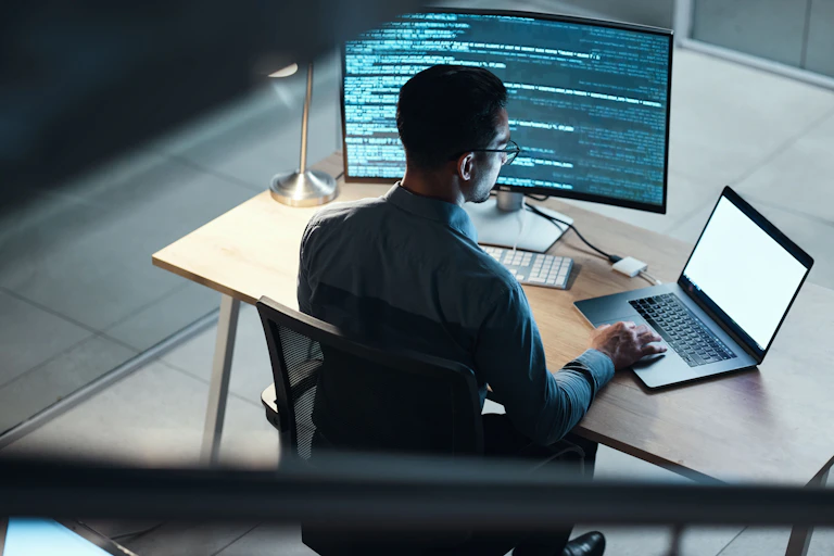 Man coding with desktop and laptop
