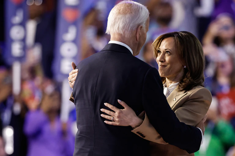 A Black woman embraces a gray-haired white man on a stage in front of thousands of spectators.