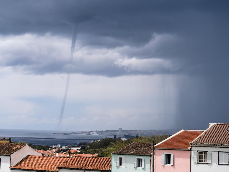 A thin column of air descending from dark storm cloud to a harbour.