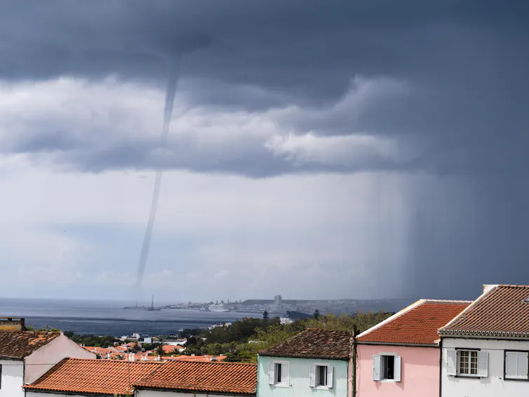 A thin column of air descending from dark storm cloud to a harbour.