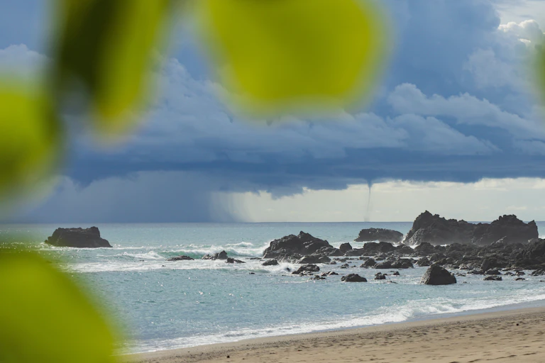 A tropical coast with a thunderstorm and waterspout in the distance.
