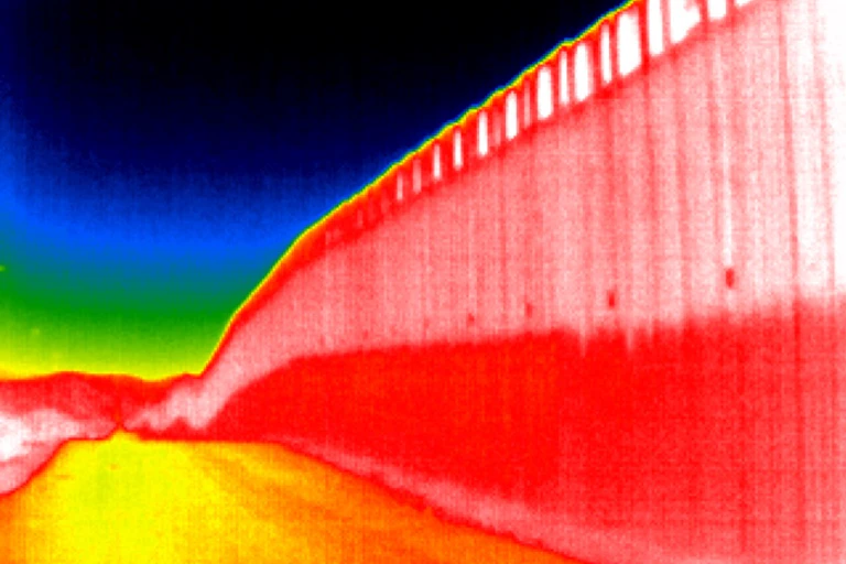 A colorful thermal image of a tall border wall with a road running parallel