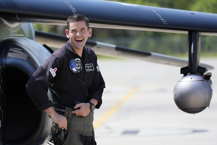 A man in a black shirt stands in front of a plane.