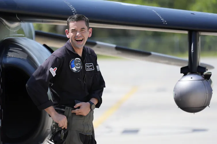A man in a black shirt stands in front of a plane.