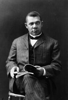 Black and white portrait of young Black man seated, wearing a suit and flipping through the pages of a book.