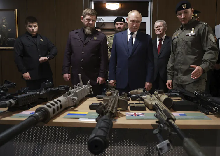 Vladimir Poutine et Ramzan Kadyrov debout devant une table où l’on aperçoit des armes