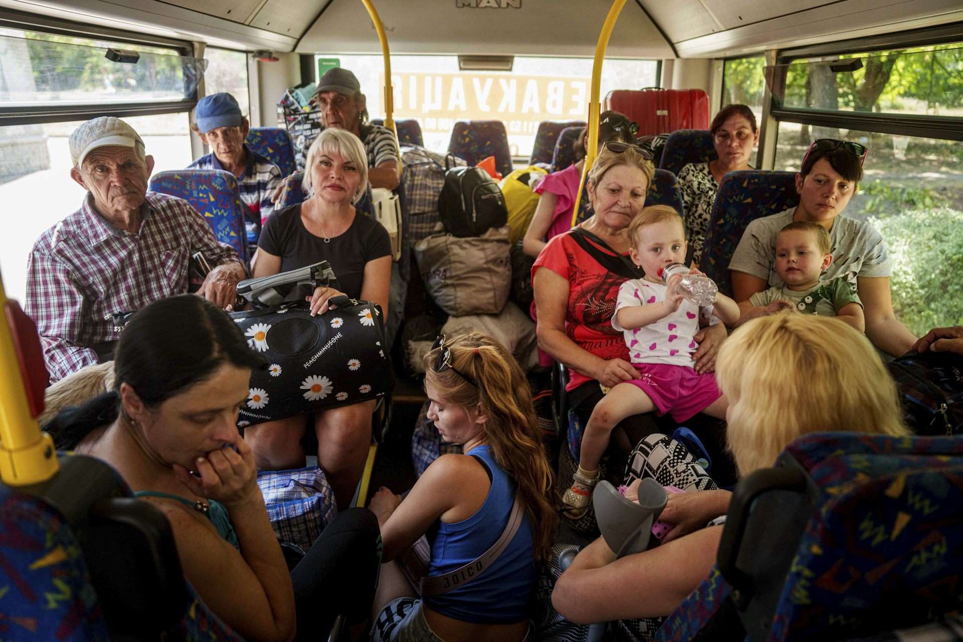 Un groupe de personnes, adultes en enfants, sont debout ou assis dans un autobus bondé